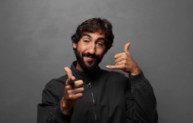 Neşeli bir şekilde gülümsüyor ve telefonla konuşurken kamerayı işaret ediyor.