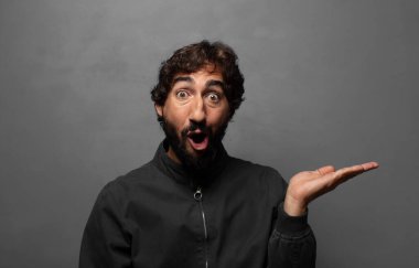 Şaşırmış ve şoke olmuş bir halde, çenesi düşmüş bir objeyi elinde açık bir elle tutarken.