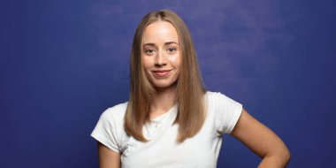 Mutlu bir şekilde gülümsüyor, eli kalçasında ve kendinden emin, olumlu, gururlu ve arkadaş canlısı bir tavırla.