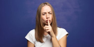 Ciddi görünüyor ve parmaklarını dudaklarına bastırıyor sessizlik ya da sessizlik talep ediyor, sır saklıyor.