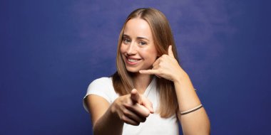 Neşeli bir şekilde gülümsüyor ve telefonla konuşurken kamerayı işaret ediyor.