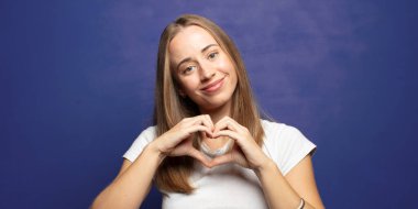 Gülümsüyor ve mutlu hissediyorum, sevimli, romantik ve aşık, her iki elinle kalbi şekillendiriyor.