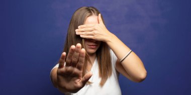 Yüzünü eliyle kapatıyor ve kamerayı durdurmak için diğer elini öne koyuyor, fotoğraf ya da resimleri reddediyor.