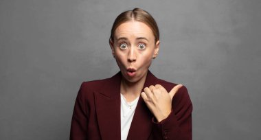 İnançsızlıktan şaşkın şaşkın bakıyor, yan taraftaki objeyi işaret ediyor ve 