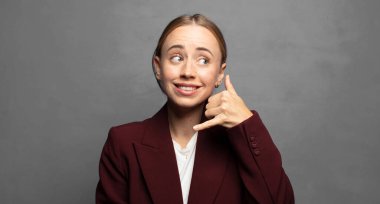 Neşeli bir şekilde gülümsüyor ve telefonla konuşurken kamerayı işaret ediyor.