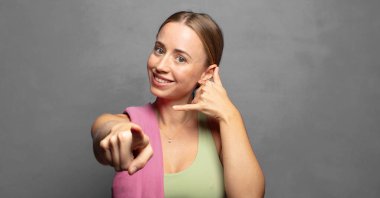 Neşeli bir şekilde gülümsüyor ve telefonla konuşurken kamerayı işaret ediyor.