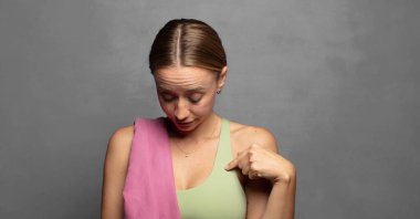 Neşeli bir şekilde gülümsüyor, aşağıya bakıyor ve göğsünü işaret ediyor.