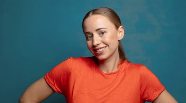 Mutlu bir şekilde gülümsüyor, elleri kalçasında ve kendinden emin, gururlu ve arkadaş canlısı bir tavırla