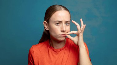 Ciddi ve hoşnutsuz görünüyor. İki parmağın önde olsun, reddedilmek üzere, sessizlik istiyorsun.