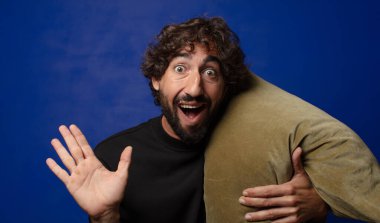 Genç sakallı çılgın adam yastığa sarılıyor.