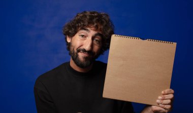 Boş defter kapağı olan genç sakallı deli adam.