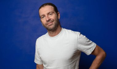 Mutlu bir şekilde gülümsüyor, eli kalçasında ve kendinden emin, olumlu, gururlu ve arkadaş canlısı bir tavırla.