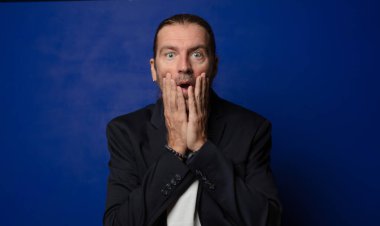 Şok olmuş ve korkmuş hissediyorum, ağzı açık ve elleri yanaklarında korkmuş görünüyor.