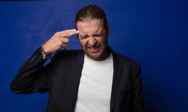 Mutsuz ve stresli görünüyor, intihar jesti elle silah işareti yapıyor, kafasını işaret ediyor.