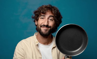 Genç, sakallı, yemek pişirme tavalı olan adam.