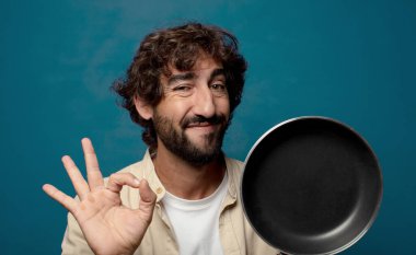 Genç, sakallı, yemek pişirme tavalı olan adam.