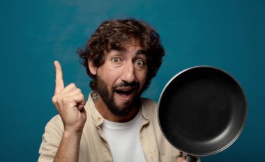 Genç, sakallı, yemek pişirme tavalı olan adam.