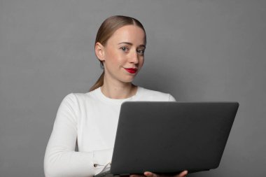 Mutlu bir şekilde gülümsüyor, eli kalçasında ve kendinden emin, olumlu, gururlu ve arkadaş canlısı bir tavırla.