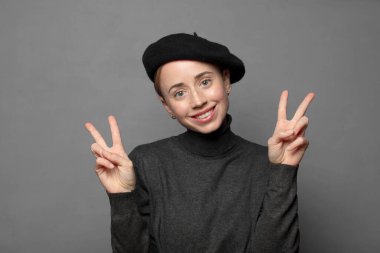 Gülümseyen ve mutlu görünen, dost canlısı ve tatmin olmuş, zafer ya da barış işareti yapan iki elinle