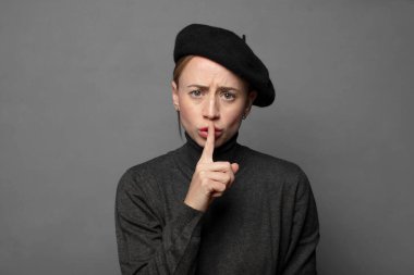 Ciddi görünüyor ve parmaklarını dudaklarına bastırıyor sessizlik ya da sessizlik talep ediyor, sır saklıyor.