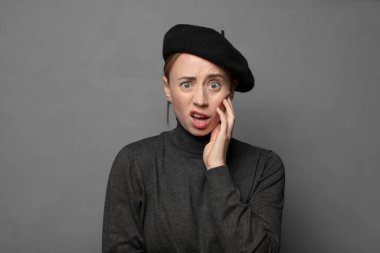 Şok ve inançsızlıkla ağzı açık, elleri yanakları ve kolları çaprazlanmış, sersemlemiş ve şaşkın.