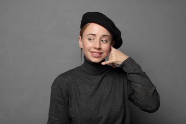 Neşeli bir şekilde gülümsüyor ve telefonla konuşurken kamerayı işaret ediyor.