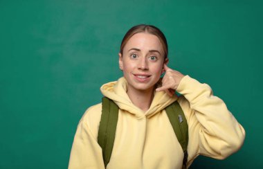 Neşeli bir şekilde gülümsüyor ve telefonla konuşurken kamerayı işaret ediyor.