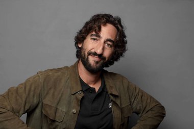 Genç sakallı adam gülümsüyor ve kameraya bakıyor.