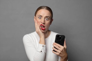 Şok ve inançsızlıkla ağzı açık, elleri yanakları ve kolları çaprazlanmış, sersemlemiş ve şaşkın.