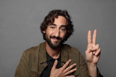 Mutlu, kendinden emin ve güvenilir görünüyor, gülümsüyor ve olumlu bir tavırla zafer işareti gösteriyor.