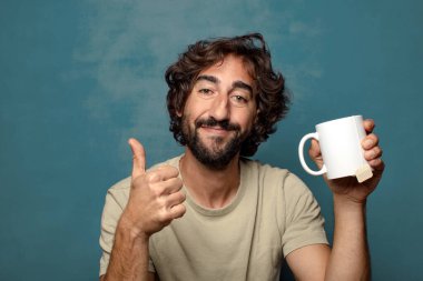 Elinde çay fincanı olan genç, sakallı bir adam.