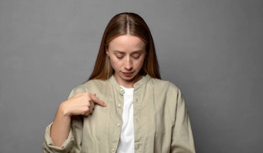 Neşeli bir şekilde gülümsüyor, aşağıya bakıyor ve göğsünü işaret ediyor.