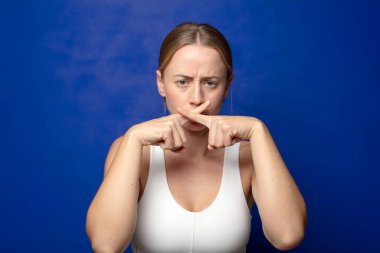 Sarışın kadın ciddi ve hoşnutsuz görünüyor. İki parmağın önde olsun, reddedilmek üzere, sessizlik istiyor.