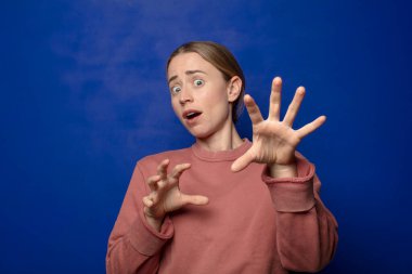 Sarışın kadın korkmuş hissediyor, korku ve panik içinde geri çekiliyor, kabusa tepki veriyor.