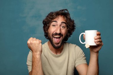 Elinde çay fincanı olan genç, sakallı bir adam.