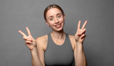 Gülümseyen ve mutlu görünen, dost canlısı ve tatmin olmuş, zafer ya da barışı simgeleyen iki elinle. fitness konsepti