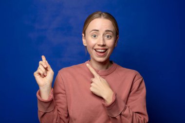 Sarışın kadın sevinçli ve şaşırmış hissediyor, şok olmuş bir ifadeyle gülümsüyor ve bir tarafı işaret ediyor.