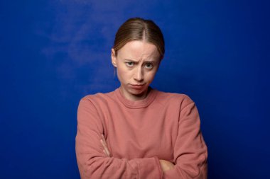 Sarışın kadın hayal kırıklığına uğramış, hayal kırıklığına uğramış, ciddi görünüyor, kızgın ve kollarını kavuşturmuş.