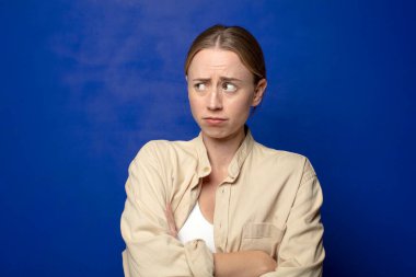 Sarışın kadın hayal kırıklığına uğramış, hayal kırıklığına uğramış, ciddi görünüyor, kızgın ve kollarını kavuşturmuş.