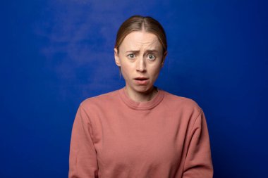 Sarışın kadın korkmuş ve şok olmuş hissediyor, ağzı açık şaşkınlık içinde.