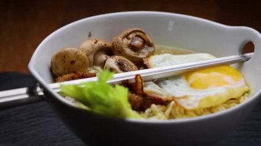 Çin yemeği çubukları Asya ramen kasesinin içine konur. Yumurta, mantar, et parçaları ve kereviz yapraklarıyla süslenir.