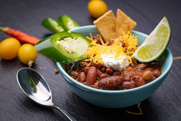 stock image Small bowl of chili garnished with jalapeo pepper slice, lime, crackers, sour cream and shredded cheese.
