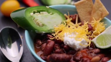 Etrafında daireler çizip duran ve ekşi krema, rendelenmiş çedar peyniri, limon dilimi, jalapeo biber dilimi ve krakerle süslenmiş et yemeği..