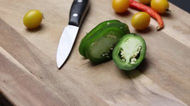 Tahta üzerinde sarı kiraz domatesleri dilimlenmiş jalapeo biberi ve mutfak bıçağı etrafında kesme tahtası