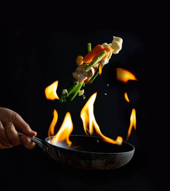 Aşçı tavada yemek, ateş ve sebze pişiriyor..