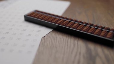 An abacus and practice printouts placed on a desk for learning how to add and multiply large numbers