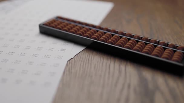 多数の足し算と掛算の方法を学ぶために机の上に置かれた算盤と練習用の印刷物 — ストック動画