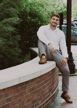 Sakallı, taş ve tuğla duvarda oturan yakışıklı bir genç.