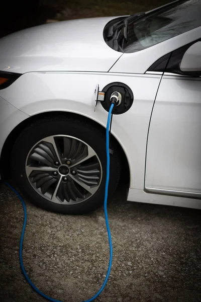 A plug in electric car is charging using a level 1 charging cable in the driveway of a residence.