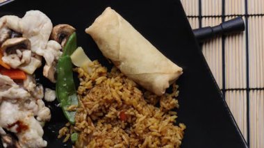 Moo Goo Gai Pan 'ın yakın çekimleri, pilav ve Çin böreğini siyah tabakta metal çubuklarla servis etmek.